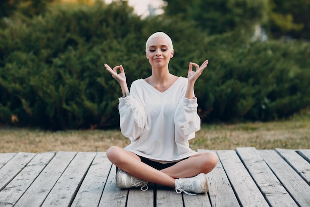 Joven milenaria rubia de pelo corto al aire libre haciendo yoga lotus