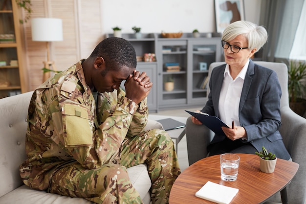 Joven militar deprimido sentado en el sofá durante la sesión de terapia con psicólogo