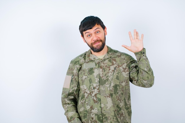 Un joven militar está mostrando un gesto de hola levantando su puñado sobre fondo blanco.