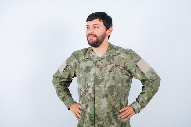 Joven militar mira a la izquierda poniendo las manos en la cintura sobre fondo blanco.