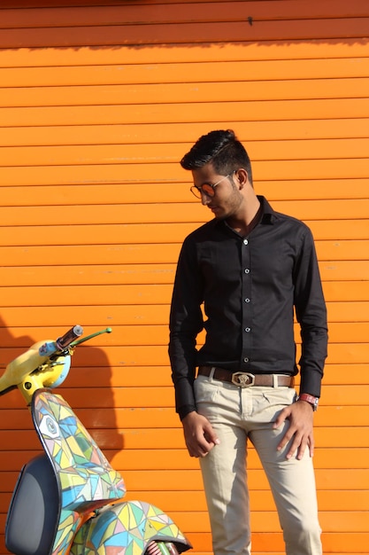 Foto joven mirando hacia otro lado mientras está de pie contra la pared naranja