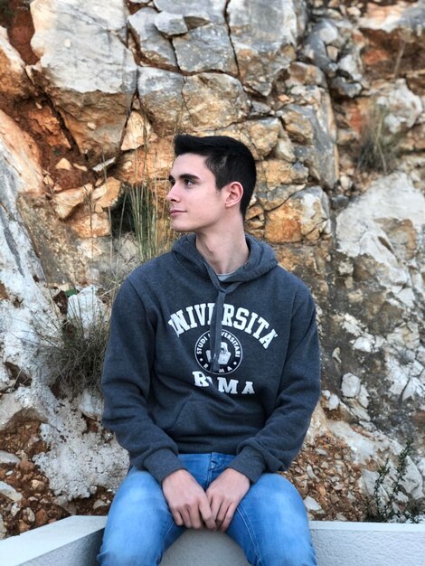 Foto joven mirando hacia otro lado mientras está sentado contra una roca