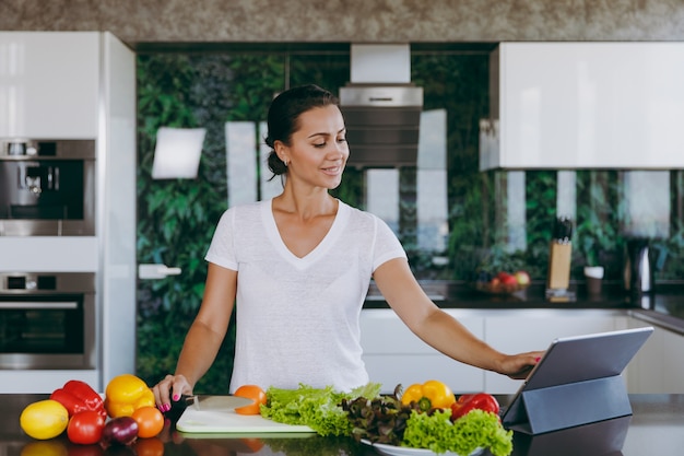 La joven mirando la receta en el portátil en la cocina