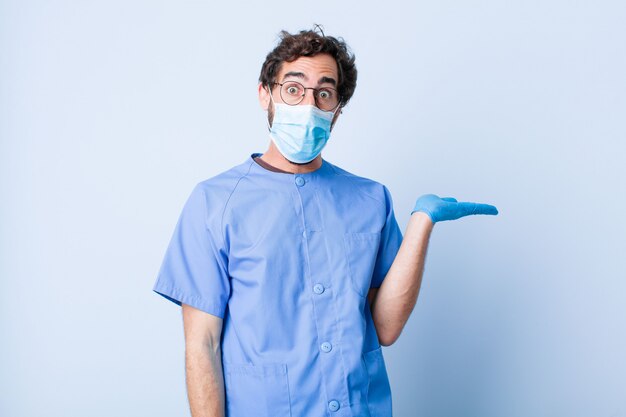 Joven mirando sorprendido y conmocionado, con la mandíbula caída sosteniendo un objeto con la mano abierta en el costado. concepto de coronavirus