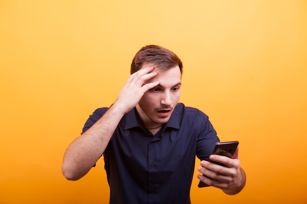 Joven mirando sorprendido en su teléfono sobre fondo amarillo. Expresión guau