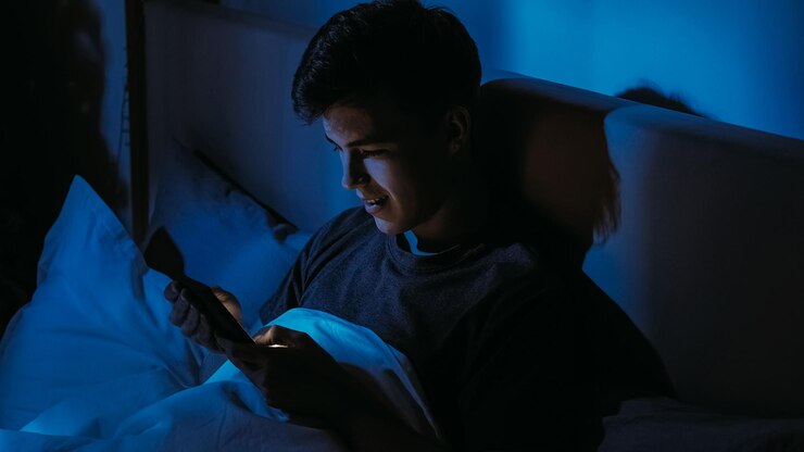 Foto un joven mirando su teléfono inteligente en la cama por la noche bajo el resplandor azul de la tecnología que refleja