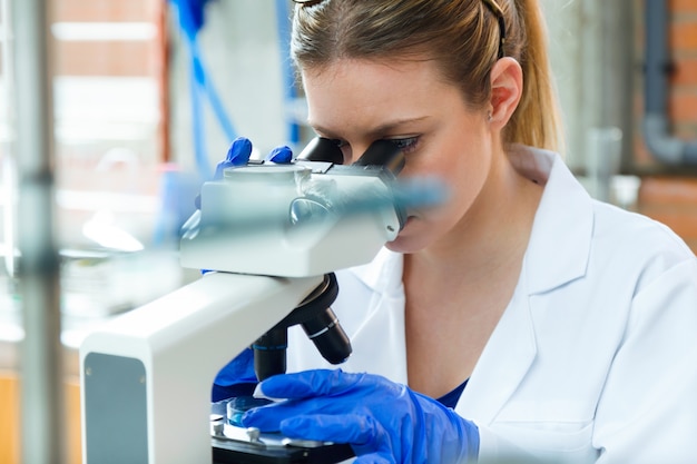 Foto joven mirando a través de microscopio en el laboratorio.