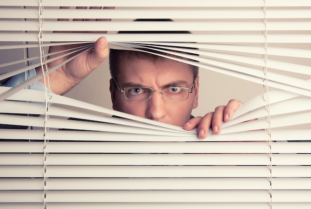 Un joven mirando a través de las persianas de la ventana