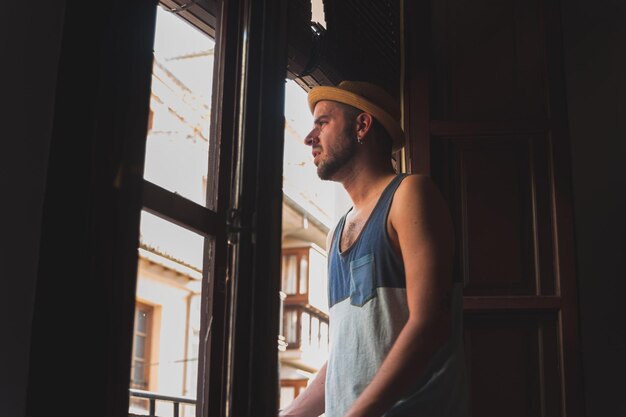 Foto joven mirando por la ventana de su casa