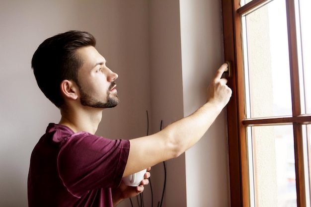 Foto un joven mirando por la ventana de su casa.