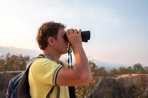 Un joven con una mochila en la espalda observa a través de binoculares desde la altura de las montañas