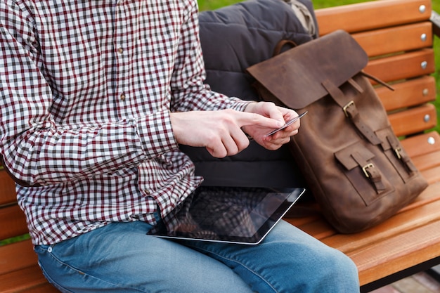 Joven con una mochila está sentado en un parque con tarjeta de crédito y tableta