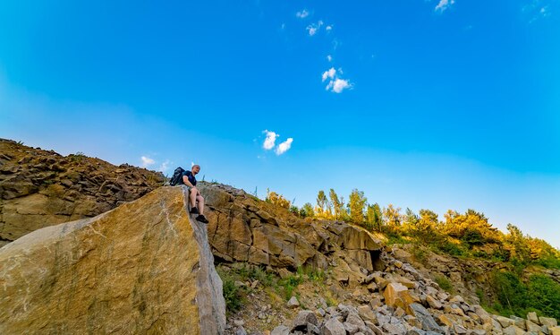 Joven con mochila sentado en el borde de un acantilado en la cima de la montaña con una hermosa vista Primer plano