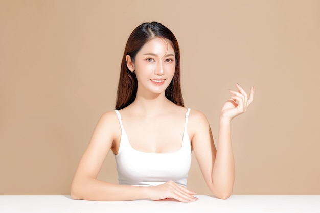 Joven modelo de belleza asiática de cabello largo con estilo de maquillaje coreano en la cara y piel perfecta en un fondo beige aislado Tratamiento facial Cosmetología Spa Cirugía plástica estética