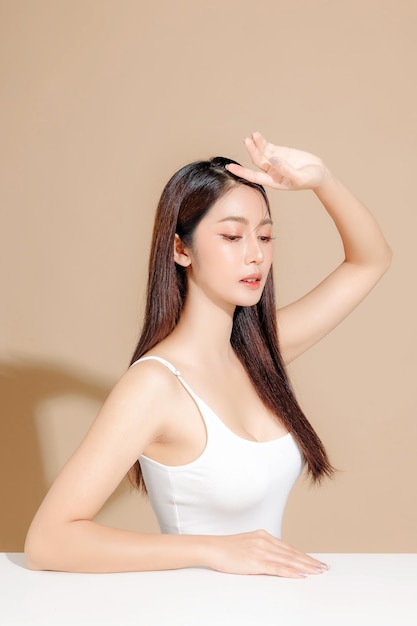 Joven modelo de belleza asiática de cabello largo con estilo de maquillaje coreano en la cara y piel perfecta en un fondo beige aislado Tratamiento facial Cosmetología Spa Cirugía plástica estética