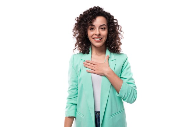 Joven modelo caucásica con el cabello rizado hasta los hombros vestida con una chaqueta azul sonriendo en un