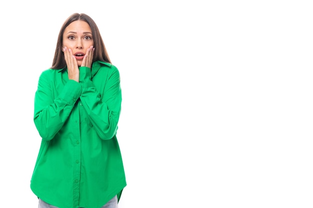 joven modelo femenino de cabello marrón con ojos marrones en una camisa verde se sorprende en un fondo blanco con espacio de copia para el texto