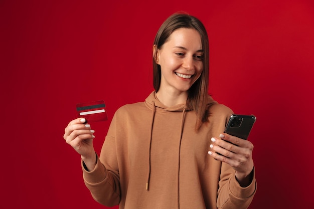 La joven moderna usa la banca móvil mientras sostiene el teléfono y su tarjeta