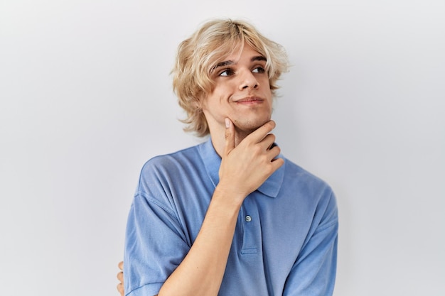 Joven moderno parado sobre un fondo aislado con la mano en la barbilla pensando en la pregunta, expresión pensativa. sonriendo con cara pensativa. concepto de duda.