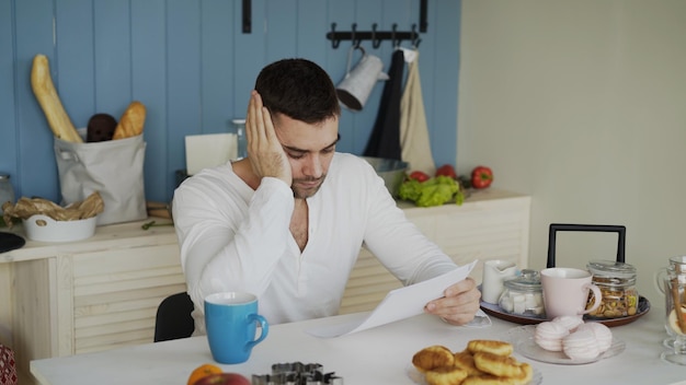 Un joven molesto leyendo una carta con una factura sin pagar en la cocina de casa