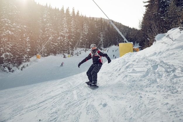 Joven monta snowboard y disfruta de un soleado día de invierno en las laderas de las montañas.