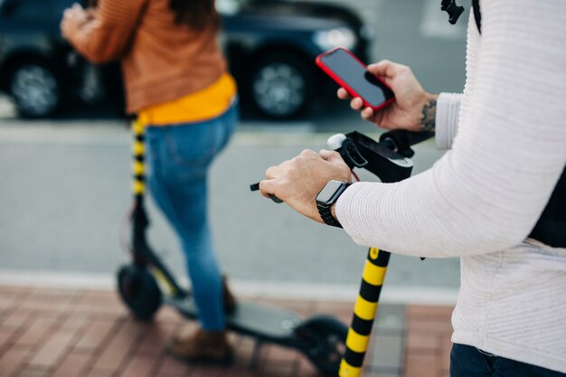 Joven montando su scooter eléctrico y mirando el teléfono móvil.