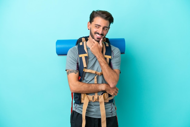 Joven montañero con una gran mochila aislada de fondo azul mirando hacia un lado