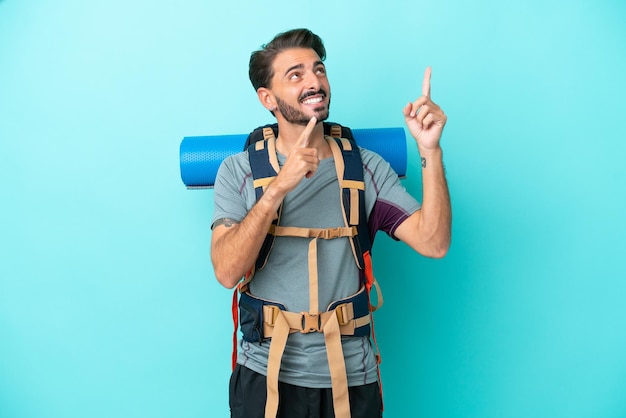 Joven montañero con una gran mochila aislada de fondo azul señalando con el dedo índice una gran idea