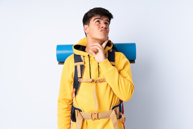 Joven montañero con una gran mochila sobre pared azul pensando en una idea