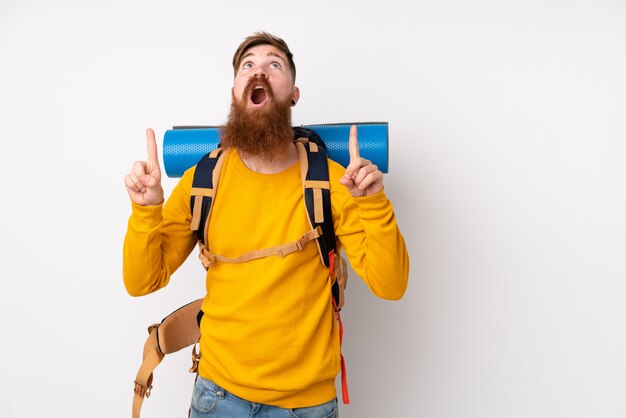 Joven montañero con una gran mochila sobre pared blanca aislada señalando con el dedo índice una gran idea