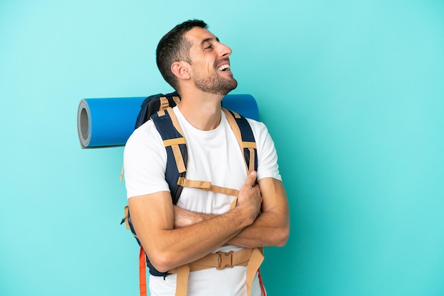 Joven montañero hombre caucásico con una mochila grande aislado sobre fondo azul feliz y sonriente