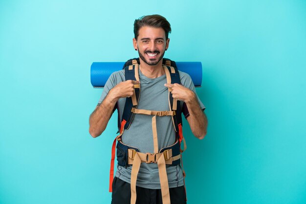 Joven montañero con una mochila grande aislada de fondo azul con expresión facial sorpresa