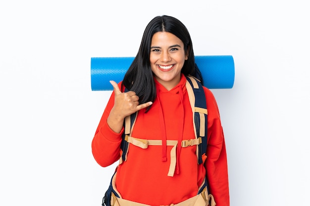 Joven montañero con una mochila grande en la pared blanca haciendo gesto de teléfono