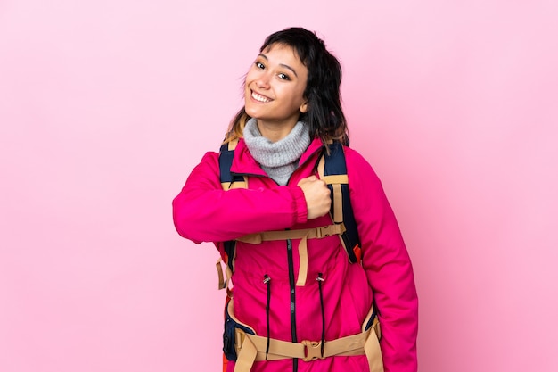 Joven montañero con una mochila grande en rosa aislado celebrando una victoria