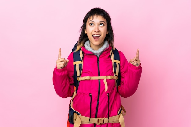 Joven montañero con una mochila grande sobre rosa aislado señalando con el dedo índice una gran idea