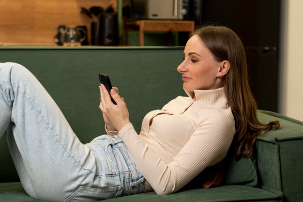 Foto una joven morena se acuesta en un sofá verde y usa un teléfono inteligente para hacer compras