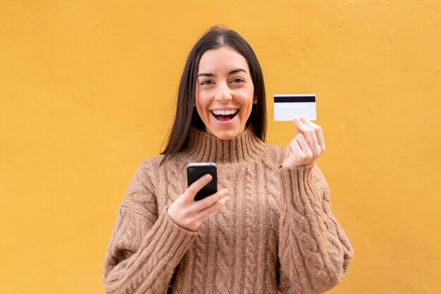 Joven morena al aire libre comprando con el móvil con tarjeta de crédito