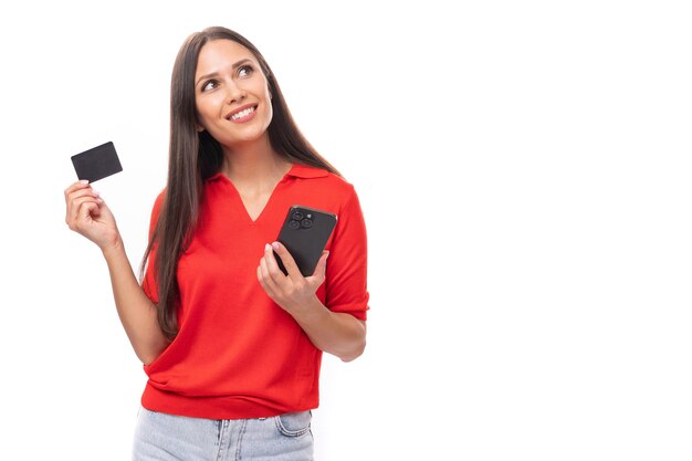 Foto una joven morena bastante caucásica con una camisa roja de manga corta sostiene una tarjeta de plástico en la mano