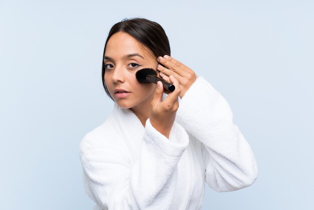 Joven morena en bata de baño con maquillaje sobre pared azul aislado