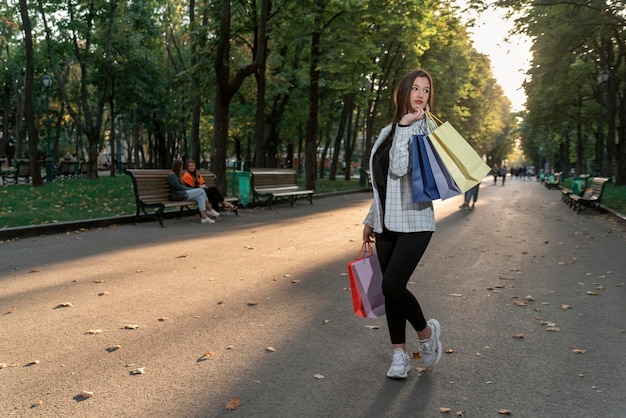 Joven morena con bolsa de compras de papel en el fondo del parque verde Después de compras exitosas al aire libre