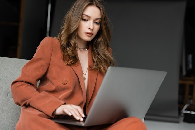 joven morena con cabello largo y collar que lleva un traje elegante de terracota con blazer y