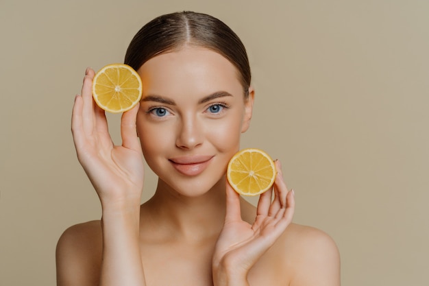 Joven morena con cabello oscuro peinado tiene dos rodajas de limones