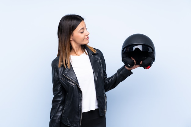 Joven morena con un casco de moto sobre pared azul con expresión feliz