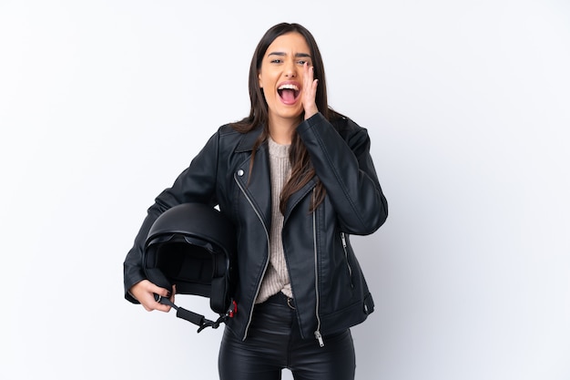 Joven morena con un casco de moto sobre pared blanca aislada gritando con la boca abierta