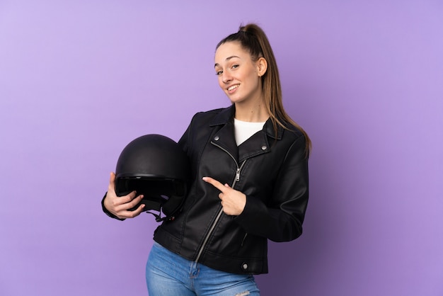 Joven morena con un casco de moto sobre pared púrpura aislado y apuntando