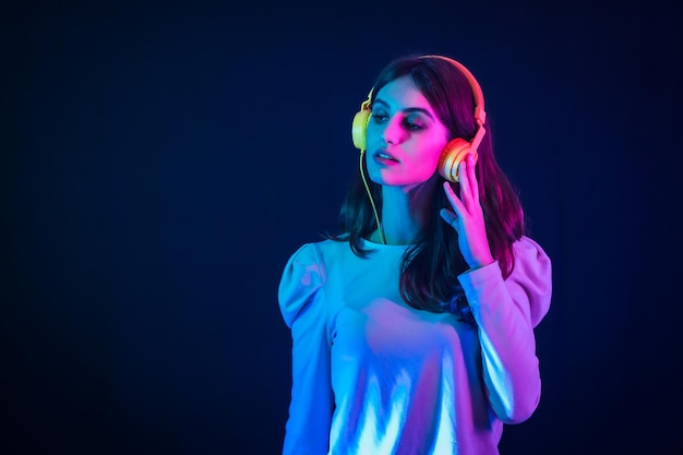 Joven morena caucásica con auriculares amarillos sobre un fondo negro, iluminado en una discoteca con luces de neón