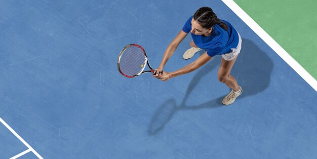 Joven morena caucásica en camisa azul jugando al tenis en la cancha. Golpea la pelota con raqueta, al aire libre. Juventud, flexibilidad, poder, energía. Copyspace. Vista superior. Movimiento, acción, estilo de vida saludable.