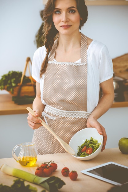 Joven morena cocinando en la cocina. Ama de casa sosteniendo una cuchara de madera en la mano. Concepto de alimentación y salud.