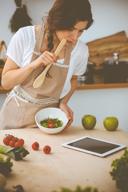 Foto joven morena cocinando en la cocina. ama de casa sosteniendo una cuchara de madera en la mano. concepto de alimentación y salud.