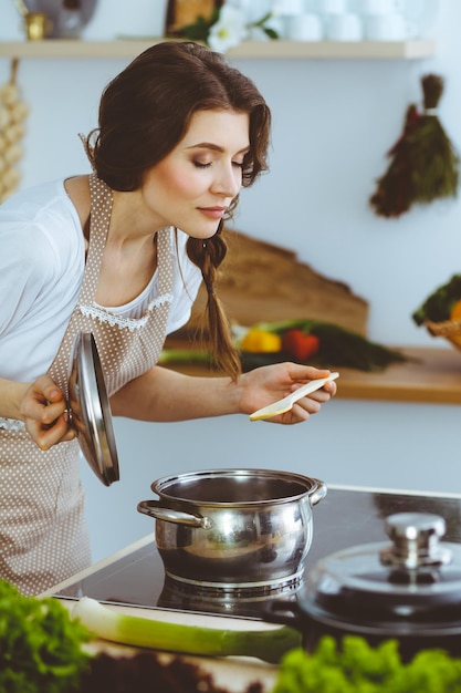 Joven morena cocinando sopa en la cocina. Ama de casa sosteniendo una cuchara de madera en la mano. Concepto de alimentación y salud.